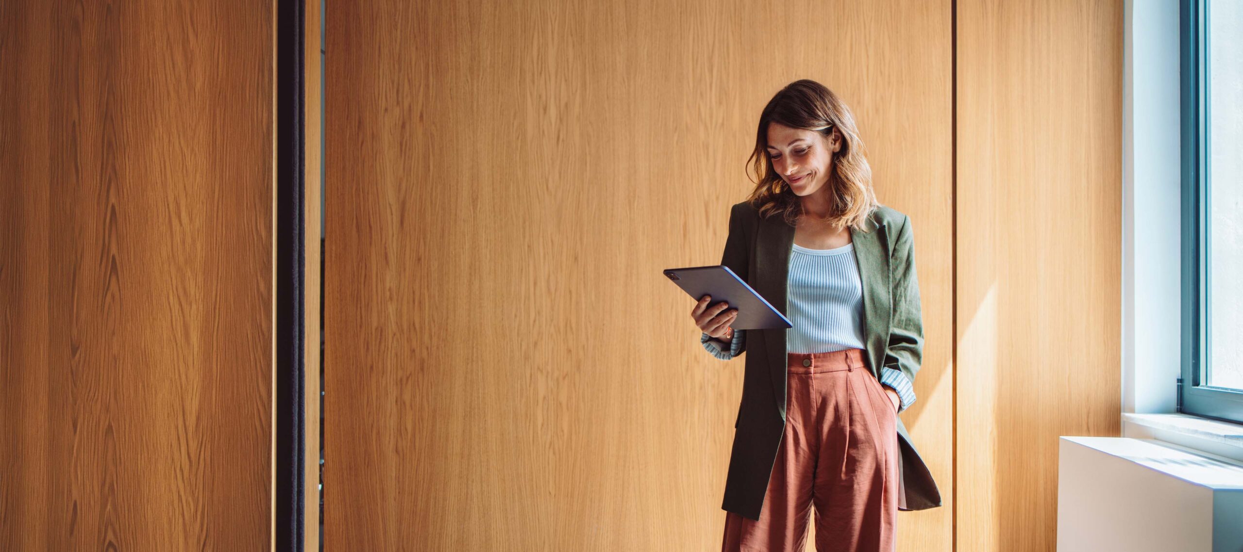 Eine Frau steht im Arbeitszimmer und schaut lächelnd auf ihr iPad